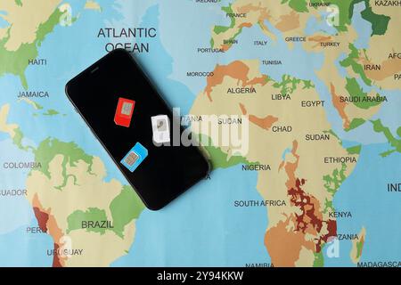 SIM cards and smartphone on world map, flat lay Stock Photo