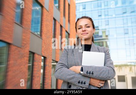 Portrait of modern businesswoman with tablet against business buildings. Stock Photo