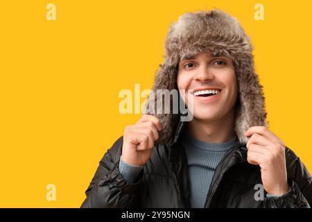 Young man in black stylish puffer jacket and hat on yellow background Stock Photo