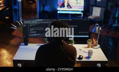 Man doing IT support job from apartment personal office drinking cup of coffee while coding. Software developer enjoying hot beverage and writing lines of code on computer, camera B Stock Photo