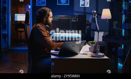 Technician typing code in neon lit personal office, using javascript programming language to develop software application. It specialist using multimonitor desktop setup to finish project, camera B Stock Photo