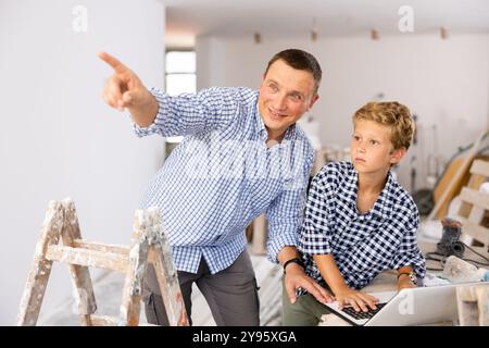 Man architect and boy using laptop while discussing working process in house being renovated Stock Photo