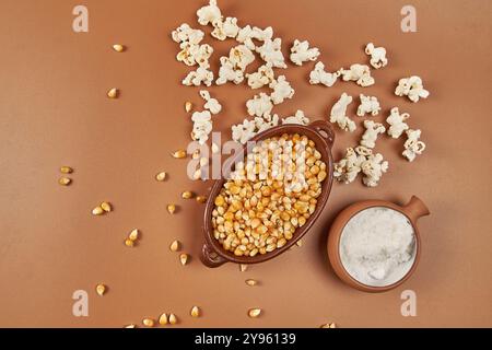 Golden corn kernels in a rustic ceramic container, the main ingredient for preparing crunchy popcorn, accompanied by a jar of salt Stock Photo