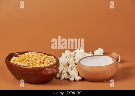 Golden corn kernels in a rustic ceramic container, the main ingredient for preparing crunchy popcorn, accompanied by a jar of salt Stock Photo