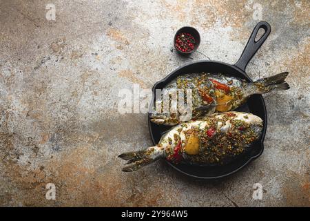 Two raw fishes dorado stuffed with vegetables and seasonings ready to be cooked laying in black cast iron frying pan top view, space for text. Healthy Stock Photo