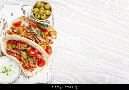Traditional Greek Dish Gyros: Pita bread Wraps with vegetables, meat, herbs, olives on rustic wooden cutting board with Tzatziki sauce, olive oil top Stock Photo