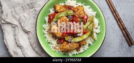 Asian sweet and sour sticky chicken with vegetables stir-fry and rice in ceramic bowl with chopsticks top view on gray rustic stone background, tradit Stock Photo