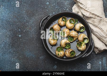 Escargots de Bourgogne Snails with Garlic Butter and Parsley in black cast iron pan on rustic stone background top view, traditional French Delicacy, Stock Photo