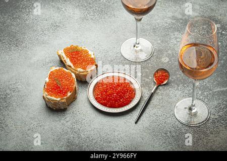 Small metal plate with red salmon caviar, two caviar toasts canape, two glasses of champagne top view on grey concrete background, festive luxury deli Stock Photo