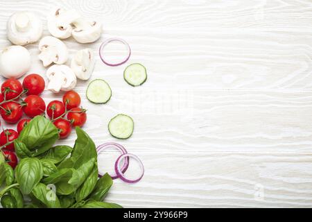 Food cooking background: fresh ingredients basil, cherry tomatoes, mushrooms, cut cucumber and onion on white wooden background top view. Meal prepari Stock Photo