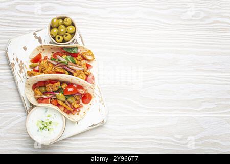Traditional Greek Dish Gyros: Pita bread Wraps with vegetables, meat, herbs, olives on rustic wooden cutting board with Tzatziki sauce, olive oil top Stock Photo