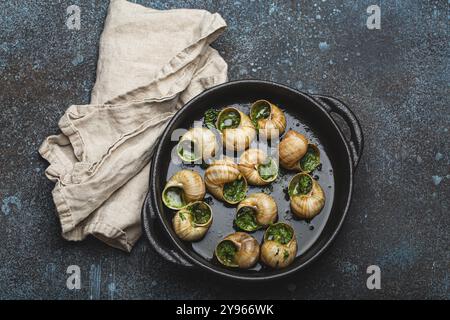 Escargots de Bourgogne Cooked Snails with Garlic Butter and Parsley in black cast iron pan on rustic stone background top view, traditional French Del Stock Photo