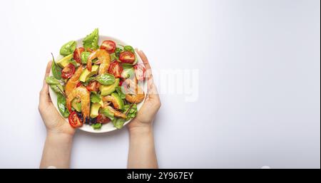 Female hands holding salad with grilled shrimps, avocado, vegetables, green leaves on white plate isolated on white background top view. Clean eating Stock Photo