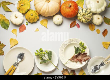 Thanksgiving festive table composition with different colourful pumpkins, autumn leaves, empty plates with cutlery on light grey background table read Stock Photo