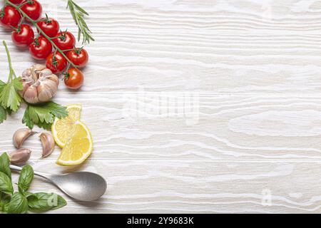 Healthy food ingredients composition with fresh cherry tomatoes, herbs, garlic cloves, lemon wedges and spoon on white wooden rustic background, overh Stock Photo