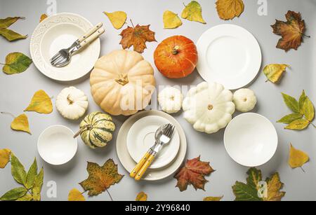Thanksgiving festive table composition with different colourful pumpkins, autumn leaves, empty plates with cutlery on light grey background table read Stock Photo