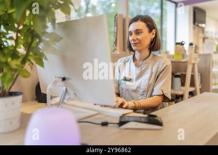 Young female pharmacist using computer sitting in the counter of a modern pharmacy store Stock Photo