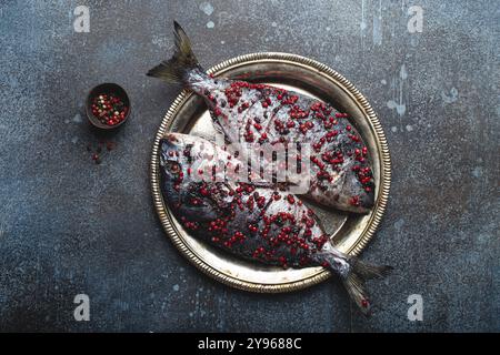 Two raw fishes dorado seasoned in pink peppercorn ready to be cooked laying on rustic metal plate top view. Healthy cooking, diet food eating concept. Stock Photo