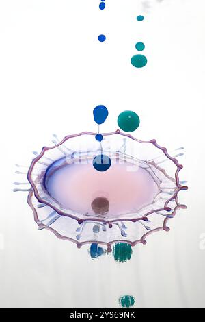 Water drop impact. High-speed photograph of secondary drop formation following the impact of a water droplet on water. The impact causes the surface of the pool to collapse, creating a rush of water inwards and upwards to form a column. Surface tension effects along the column cause a secondary drop to form. Shock waves radiate outwards as concentric circular ripples. Stock Photo