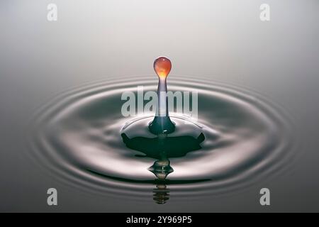 Water drop impact. High-speed photograph of secondary drop formation following the impact of a water droplet on water. The impact causes the surface of the pool to collapse, creating a rush of water inwards and upwards to form a column. Surface tension effects along the column cause a secondary drop to form. Shock waves radiate outwards as concentric circular ripples. Stock Photo
