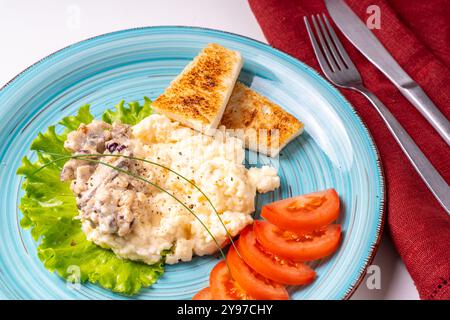 Scrambled eggs with mushrooms and crispy toast, garnished with lettuce and tomatoes, on a turquoise plate, on a white table with a burgundy napkin and Stock Photo