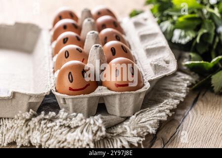 Cute smiling fresh eggs in a paper carton on the kitchen table. Stock Photo