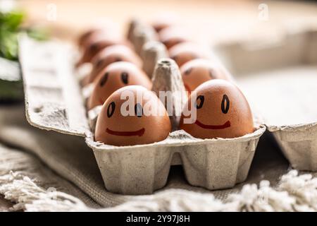 Cute smiling fresh eggs in a paper carton on the kitchen table. Stock Photo
