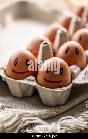Cute smiling fresh eggs in a paper carton on the kitchen table. Stock Photo