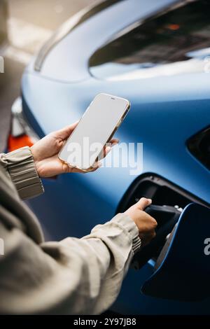 Woman connects their electric car to a charging station while using a smartphone. This image conveys modern technology, sustainability, and environmen Stock Photo