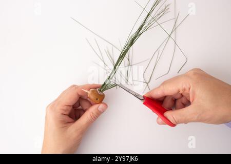 step in creative process, DIY, autumn craft, handmade bird crafted from pine cones and twigs, the head appears to be an acorn, hands cutting with scis Stock Photo