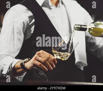 Sommelier pours white wine to wineglass on bar counter background, close-up view. Stock Photo