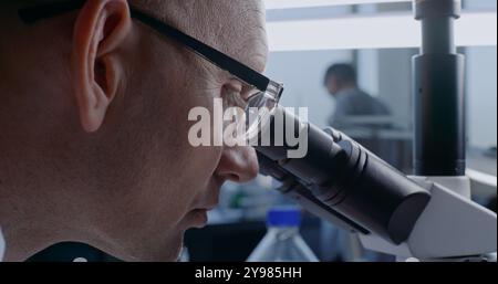 In bright medical laboratory: Professional microbiologist looking under microscope, analyzing samples. Male scientist working, using high-tech equipment. Modern technologies in medicine. Close up. Stock Photo