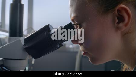 In medical laboratory, female microbiologist looks under microscope at samples, does analysis. Scientific method of research at work. Pharmaceutical discoveries. Development of medicine. Close up. Stock Photo