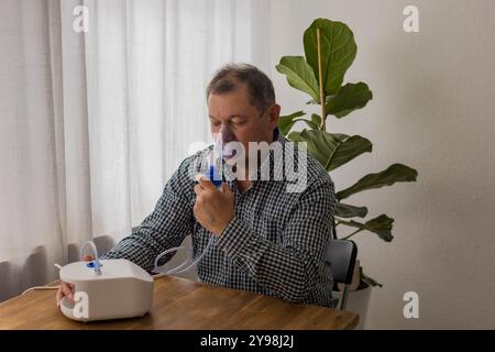 Elderly man sitting on a table and using a nebulizer mist at home. High quality photo Stock Photo