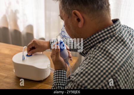 Elderly man sitting on a table and using a nebulizer mist at home. High quality photo Stock Photo