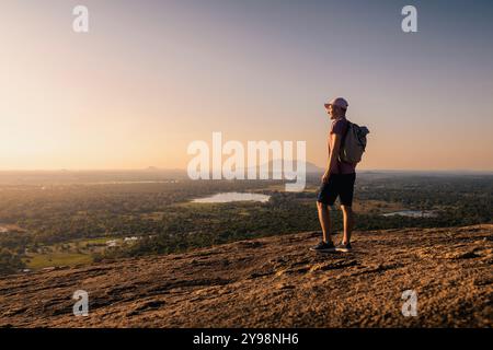 Man with backpack on top of rock looking at landscape at sunset. Beautiful scenery in Sri Lanka. Stock Photo