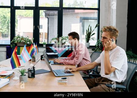 A beautiful couple collaborates at a stylish desk, showcasing pride flags while working diligently. Stock Photo