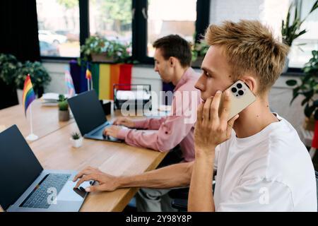 Two men engage in focused work at a lively office adorned with pride flags and plants. Stock Photo
