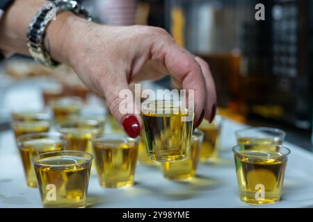 Woman is picking up a shot glass filled with alcohol from a tray of similar drinks at a party. Selective focus Stock Photo