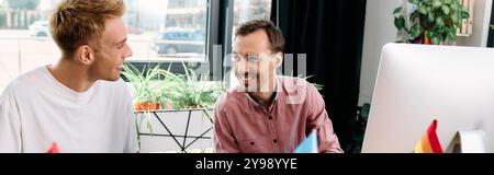 Two smiling men share a light hearted conversation while working together in a bright room. Stock Photo