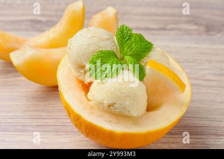 Scoops of tasty melon sorbet with mint in fresh fruit on wooden table, closeup Stock Photo