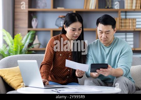 Couple managing finances at home using calculator and laptop, focusing on budgeting and expense tracking for responsible financial planning, teamwork, and collaboration. Stock Photo