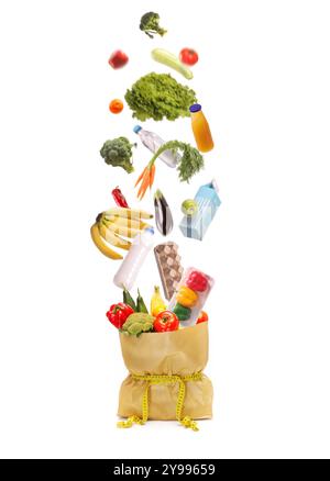 Studio shot of fresh fruits and vegetables falling into a paper bag with a measuring tape isolated on white background Stock Photo