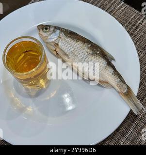 A shot glass of alcohol and dried fish on a white plate. Stock Photo