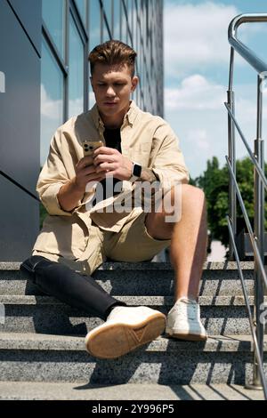 A dedicated young man using his smartphone while seated on stairs in a contemporary office environment. Stock Photo