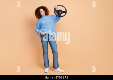 Photo of young car driver girl enjoy her new automobile holding leather steering wheel isolated on beige color background Stock Photo