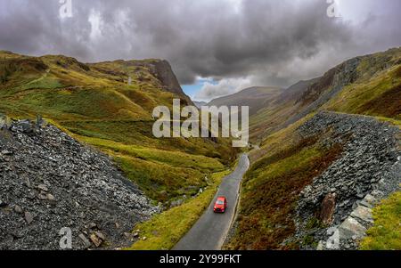 A landscape view of a car reaching the top of the B5289 Honister Pass road from The Honister Slate Mine in The English Lake District National Park on Stock Photo