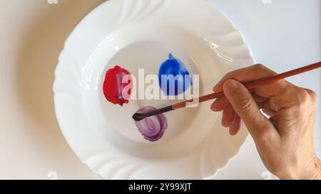 Mixing purple watercolor on a plate using red and blue colors, close-up view Stock Photo