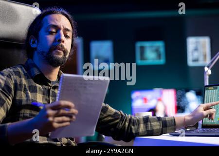 Determined man working diligently at his desk using laptop and pen, researching, and brainstorming ideas. Productive and focused male individual utilizing notebook and technology for work and study. Stock Photo