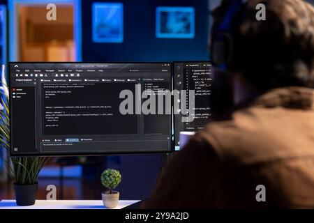 Man doing software quality assurance, reading source code on computer screen before implementing it. Developer inspecting coding on desktop PC, looking to fix potential issues Stock Photo